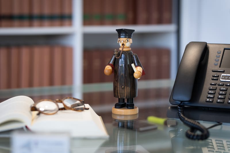 Kleine Holzfigur eines Anwalts in Robe neben einem aufgeschlagenen Buch und einem Telefon